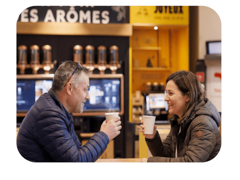 Couple profitant d’un café offert en station‑service TotalEnergies, partageant un moment convivial devant le comptoir des arômes